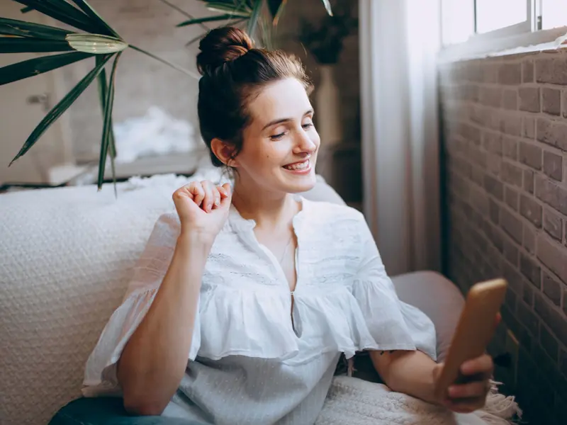 Une femme utilise son téléphone, assise sur un canapé.